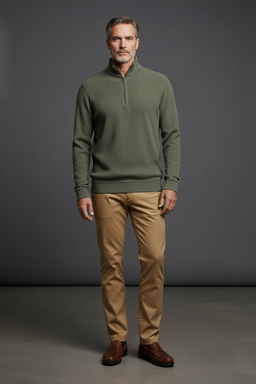 Man wearing a green sweater and white pants against a gray background