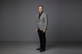Man wearing a gray checkered blazer over a white shirt with black pants on a gray background